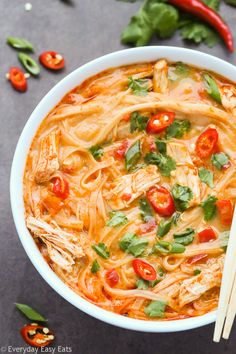 a bowl of chicken noodle soup with chopsticks and tomatoes on the side