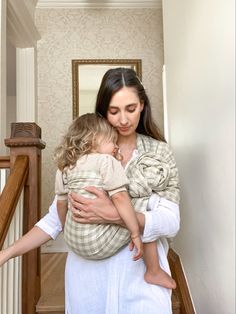 a woman holding a baby in her arms while standing on the stairs next to a mirror