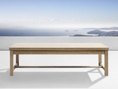 a wooden table sitting on top of a white floor next to a wall with an ocean view