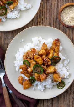 two plates filled with rice and chicken on top of a wooden table next to silverware