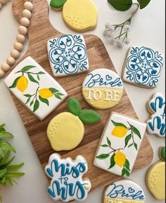 decorated cookies are on a cutting board next to some flowers and greenery, including lemons