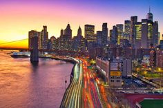 the city skyline is lit up at night, with cars driving on the road and bridge in the foreground