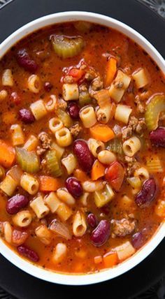 a bowl filled with pasta and vegetables on top of a black table next to a spoon