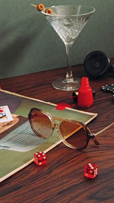 a pair of glasses sitting on top of a wooden table next to dice and cards