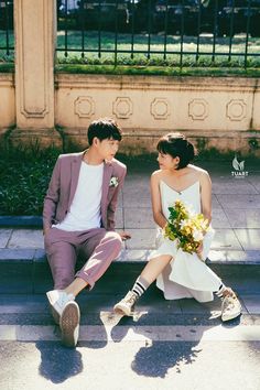 a man and woman sitting on the ground next to each other with flowers in their hands