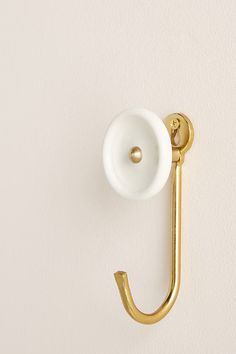 a gold hook on the wall with a white cup hanging from it's side