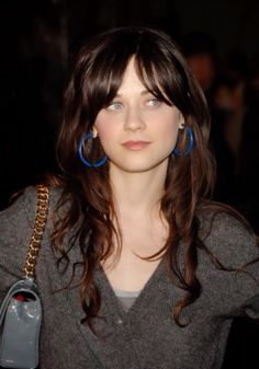 a woman with long hair and blue hoop earrings is looking at the camera while wearing a gray sweater