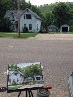 an easel with a painting on it sitting in the street next to a car