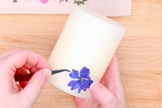 someone is decorating a candle with blue flowers on the outside and inside it, while another hand holds a small flower