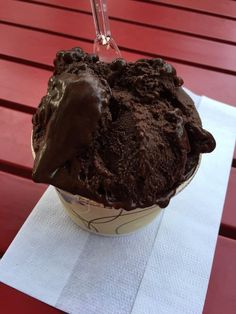 an ice cream sundae with chocolate icing on a red wooden table top,