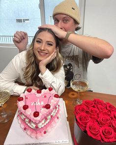 a man and woman sitting at a table with a heart shaped cake in front of them