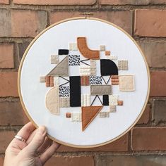 someone is holding up a cross stitch pattern on a white hoop with black and orange shapes