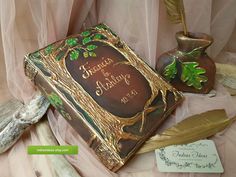 there is a book that has been decorated with leaves and branches on the cover, next to a feather quill