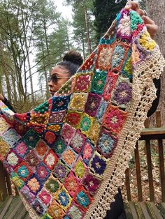 a woman holding up a colorful crocheted blanket