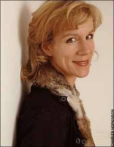 a woman with blonde hair wearing a black jacket and fur collar smiling at the camera