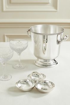 a silver ice bucket sitting on top of a white table next to two wine glasses