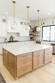 a large kitchen with white cabinets and gold accents on the island countertop, along with brass pendant lights