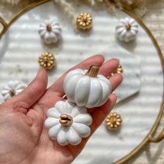 a hand holding two white pumpkins on top of a plate next to other decorations