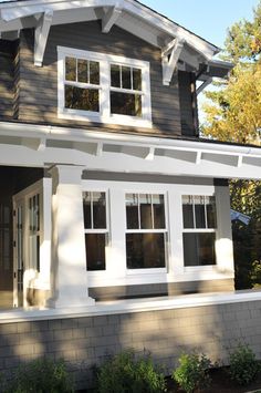 a gray house with white trim on the front and side windows is shown in this image