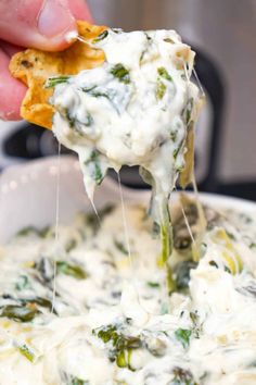 a hand holding a tortilla chip and dipping it into a white bowl filled with spinach dip