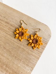 two yellow sunflowers are hanging from gold earwires on a wooden board