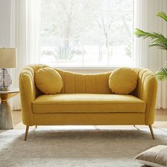 a yellow couch sitting in front of a window next to a table with a lamp on it