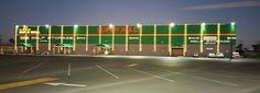 an empty parking lot in front of a large green and yellow building with lights on it