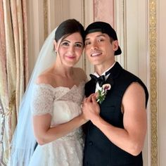 a bride and groom pose for a photo in front of a wall decorated with gold trim