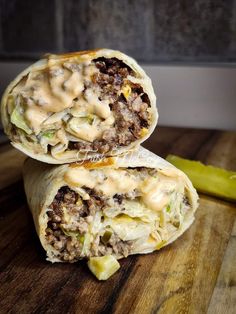 two burritos sitting on top of a wooden cutting board next to a pickle