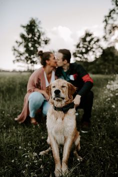 a man and woman sitting in the grass with their dog