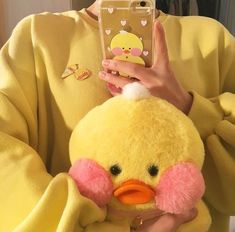 a woman holding a yellow stuffed duck in her hands and looking at the camera phone