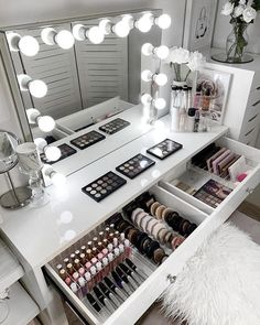 a vanity with lights and makeup on it in a room next to a mirror that has drawers full of cosmetics