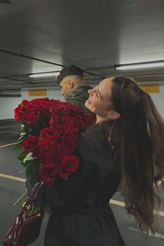 a woman holding flowers in her hand while standing next to a man with long hair