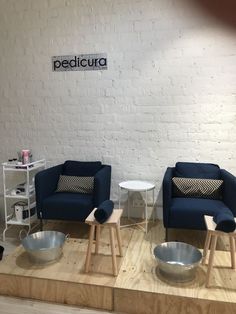 two blue chairs sitting next to each other on top of a hard wood floor in front of a white brick wall