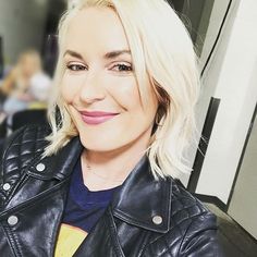 a woman with blonde hair wearing a black leather jacket and smiling at the camera while sitting down