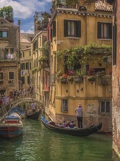 two gondolas in the water next to buildings with flowers on them and people walking along