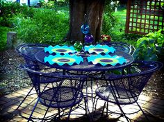 an outdoor table with blue and yellow plates on it in the middle of a garden