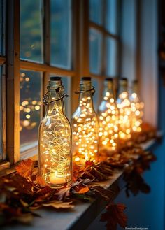 lighted bottles lined up on a window sill in front of a window with autumn leaves