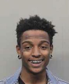 a young man with black hair and piercings smiles at the camera while wearing a denim shirt