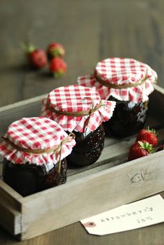 four jars of jam in a wooden box with strawberries on the table next to it