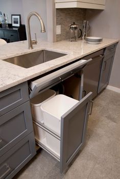 a kitchen sink with an open cabinet in the middle and a pull out trash can underneath