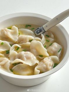 a white bowl filled with dumplings on top of a table next to a spoon