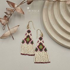 a pair of beaded earrings sitting on top of a white plate next to a plant