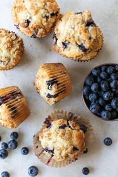 blueberry muffins and fresh blueberries on a white surface with a small bowl of blueberries