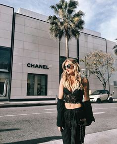 a woman standing on the sidewalk in front of a chanel store with palm trees