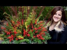 a woman standing in front of a potted plant with red berries and green foliage