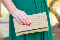 a woman in a green dress holding a gold clutch bag with her hand on it