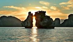 the sun is setting over some rocks in the water near an island with two large rocks sticking out of it