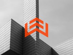 an orange and black logo on the side of a tall building with glass windows in front of it