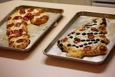 two pans with pizza on them sitting on a table next to each other,